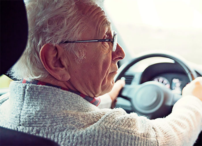 An elderly man looks to the side as he drives